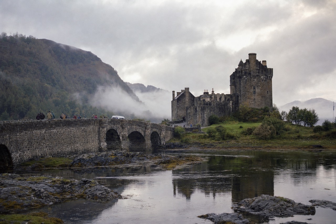 Eilean Donan Castle on its island at the meeting of three sea lochs, stone bridge in the foreground under broken cloud.